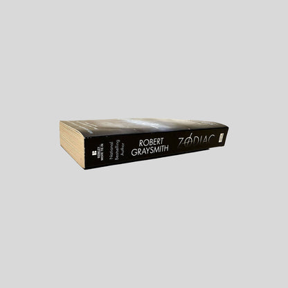 Close-up spine view of Zodiac by Robert Graysmith centered on a neutral light gray background. 