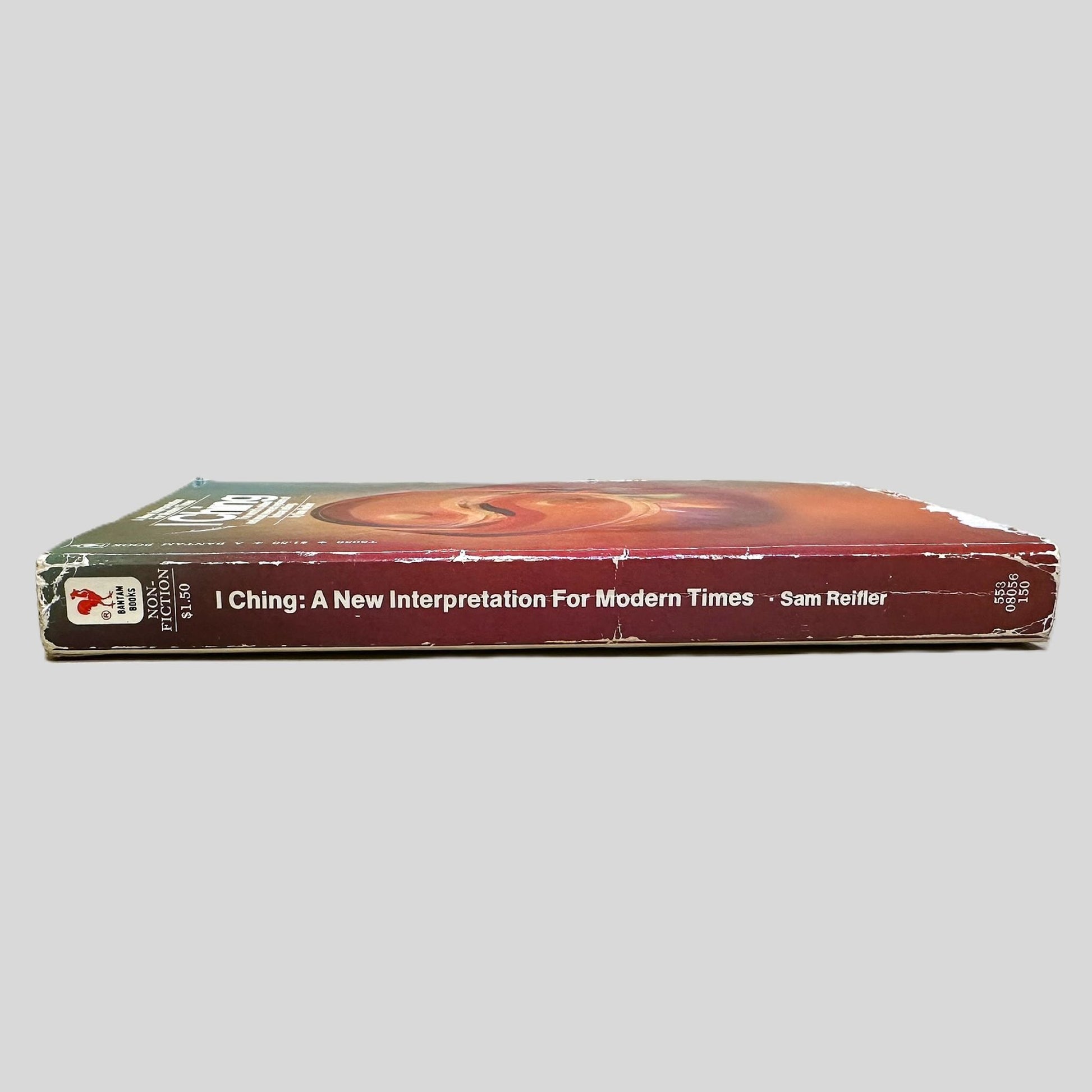 Side-angle view of the book 'I Ching' resting on a neutral background. The spine prominently displays the Bantam Books logo, the title, and the author's name, reflecting the well-read condition of this modernized ancient oracle. The screen captures the genuine vintage character and historical significance of this specific printing.