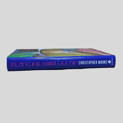 Spine and page edges of the humorous fiction book 'Island of the Sequined Love Nun' by Christopher Moore, highlighting the book's thickness and the Avon imprint on a light background.
