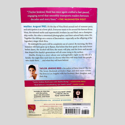The back cover of the Ballantine Books paperback edition of 'Malibu Rising' by Taylor Jenkins Reid. A vibrant pink and white background features a glowing review from The Washington Post praising the novel's 'fast-paced, engaging' storytelling. The central summary details a single unforgettable night in August 1983 when the famous Riva siblings—Nina, Jay, Hud, and Kit—throw a party that ends in flames, documenting the authentic condition of this popular summer read.