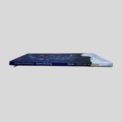 Srijon Chowdhury art exhibition catalog 'Same Old Song' displayed from the side to show the spine and page edges on a neutral gray background