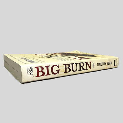 Side-angle view of 'The Big Burn: Teddy Roosevelt and the Fire that Saved America' by Timothy Egan resting on a neutral background. The screen captures the bold title and author name on the spine, reflecting the high-quality trade paperback design of Mariner Books. The layout emphasizes the historical importance of the narrative, showcasing the substantial page count and sharp corners of this renowned conservation history.