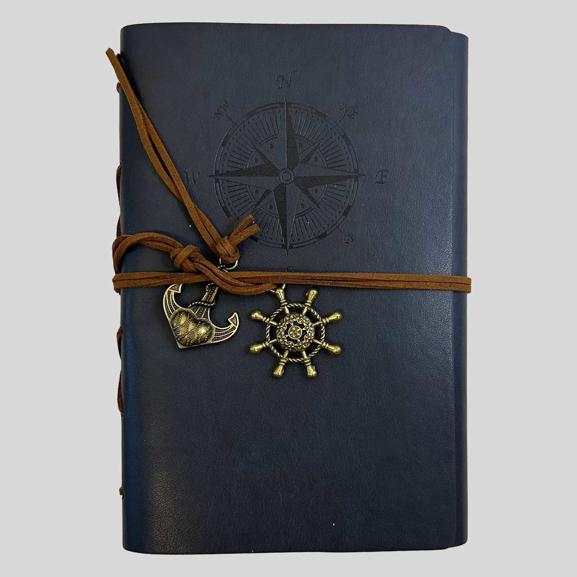 A professional product shot of a sleek black faux-leather journal from the Fehmerling Books standalone collection. The screen showcases a debossed compass rose on the cover, secured by brown twine and accented with antique gold-toned anchor and ship wheel charms. This high-quality image captures a bold, classic aesthetic, perfect for creative writing and professional note-taking.