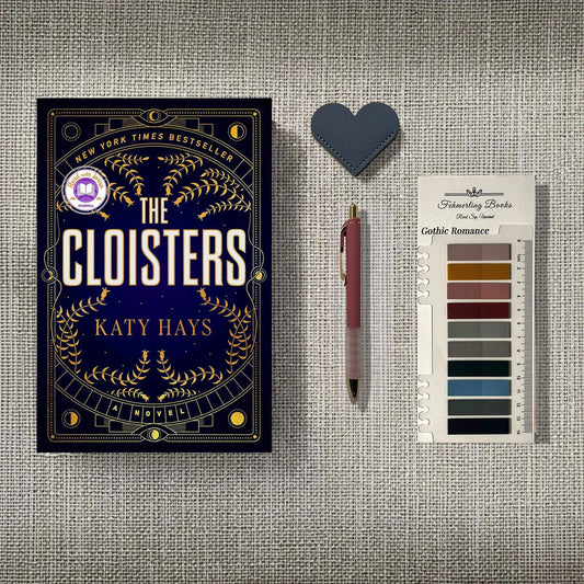 A styled flat-lay featuring the book 'The Cloisters' by Katy Hays, a pink pen, a heart-shaped leather bookmark, and Gothic Romance annotation tabs from Fehmerling Books, all arranged on a textured gray fabric background.