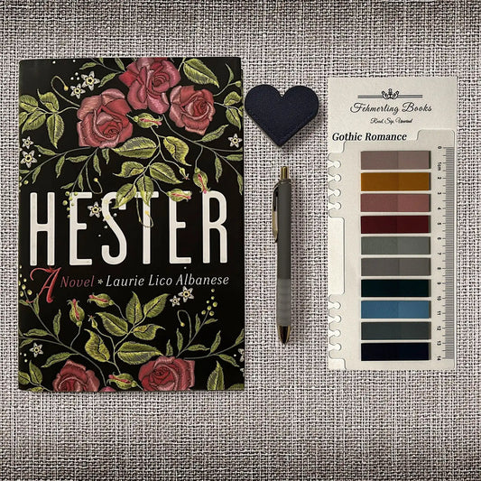 A book titled 'HESTER' by Laurie Lico Albanese is displayed on a textured gray fabric background alongside a dark blue heart-shaped bookmark, a gray pen, and Gothic Romance annotation tabs from Fehmerling Books.