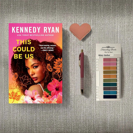 A styled flat-lay featuring the book 'This Could Be Us' by Kennedy Ryan, a pink heart-shaped leather bookmark, a pink pen, and a 'Fehmerling Books' Misty Harbor annotation tab card, arranged on a gray textured fabric background.