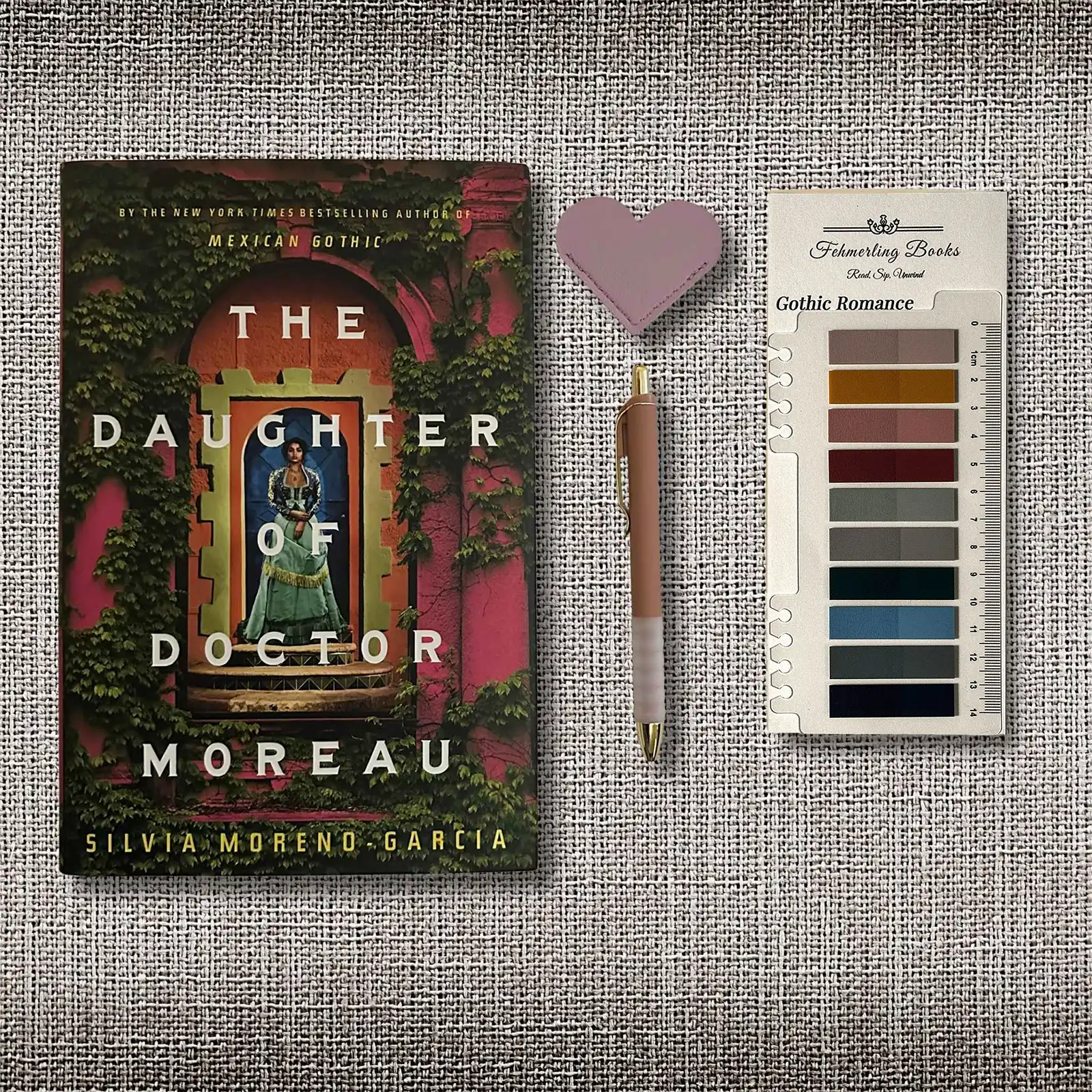 The book cover of 'The Daughter of Doctor Moreau' by Silvia Moreno-Garcia is displayed next to a heart-shaped leather bookmark, a pen and Gothic Romance annotation tabs from Fehmerling Books on a textured gray burlap background.