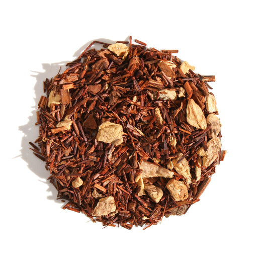 A close-up, overhead view of Plum Deluxe Gingersnap Herbal Tea arranged in a neat circle against a white background. The caffeine-free loose leaf blend features a red rooibos base heavily accented with visible pieces of dried ginger and warm cinnamon.