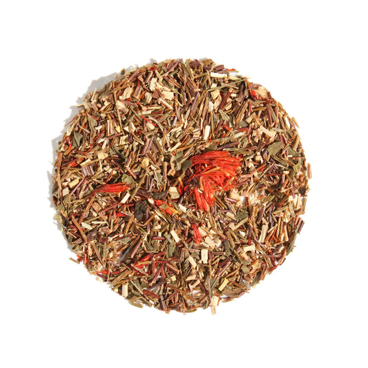 A close-up, overhead view of Plum Deluxe Candy Cane Herbal Tea arranged in a neat circle against a white background. The caffeine-free loose leaf blend features fine green rooibos and peppermint, highlighted by vivid red safflower petals.