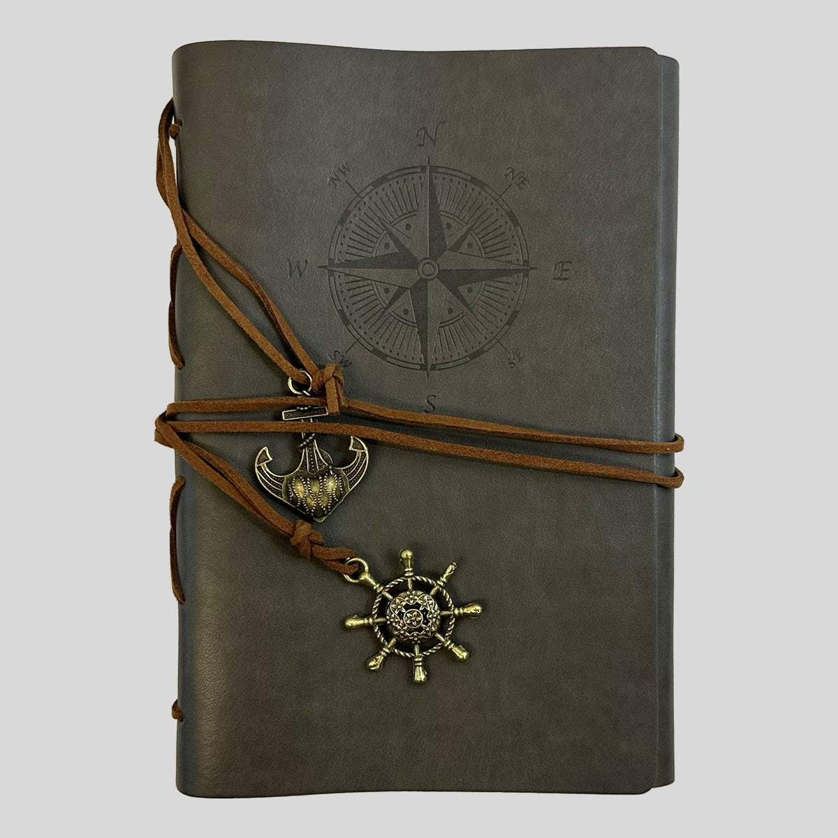 A professional product shot of a stone-grey faux-leather journal from the Fehmerling Books standalone collection. The screen showcases a debossed compass rose on the cover, wrapped with brown twine and accented by antique gold-toned anchor and ship wheel charms. This high-quality image captures a sophisticated, seafaring aesthetic, perfect for mapping thoughts or creative writing.