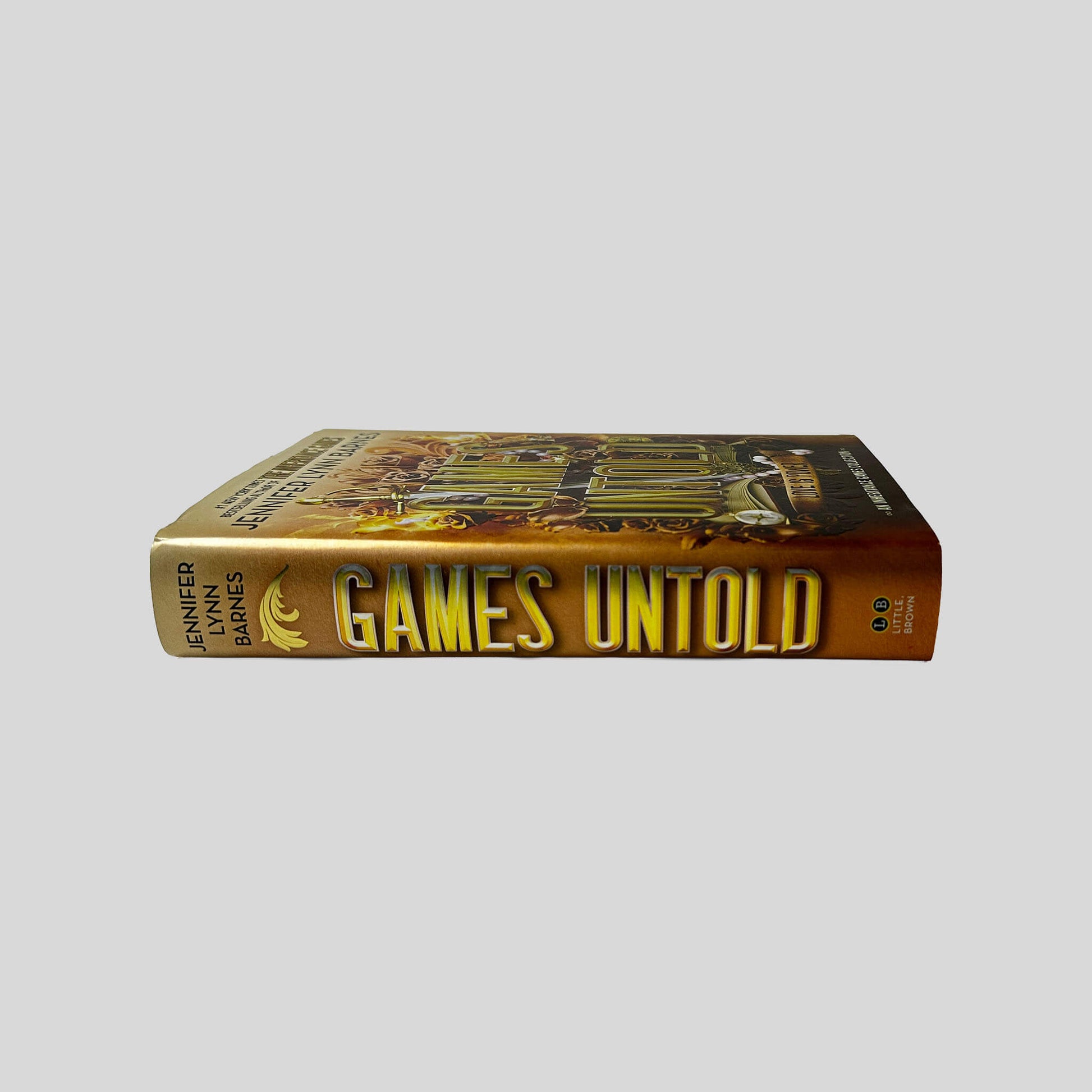 Unbroken spine view of Games Untold hardcover dust jacket by Jennifer Lynn Barnes displaying metallic gold title lettering, Little Brown publisher logo, and crisp edges.