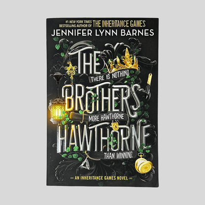 Front cover of The Brothers Hawthorne by Jennifer Lynn Barnes in Like New paperback condition, featuring bold metallic title lettering surrounded by dark green vine filigree, a glowing lantern, a gold crown, and a pocket watch.