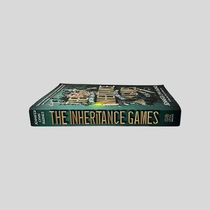 Unbroken spine view of The Inheritance Games paperback by Jennifer Lynn Barnes showing metallic gold title lettering, pristine edges, and clean binding.