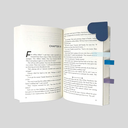 Close-up angled view of Slate Blue leather heart bookmark on open novel with Dawn to Dusk annotation tabs by Fehmerling Books.