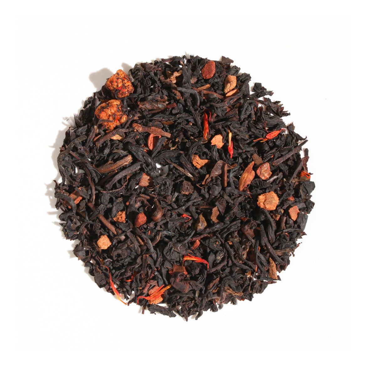 A close-up, overhead view of Plum Deluxe Maple Pecan Holiday Tea arranged in a neat circle against a white background. The loose leaf blend features dark, rolled black and oolong tea leaves accented with chunky nut pieces, spices, and vivid red and orange petals.