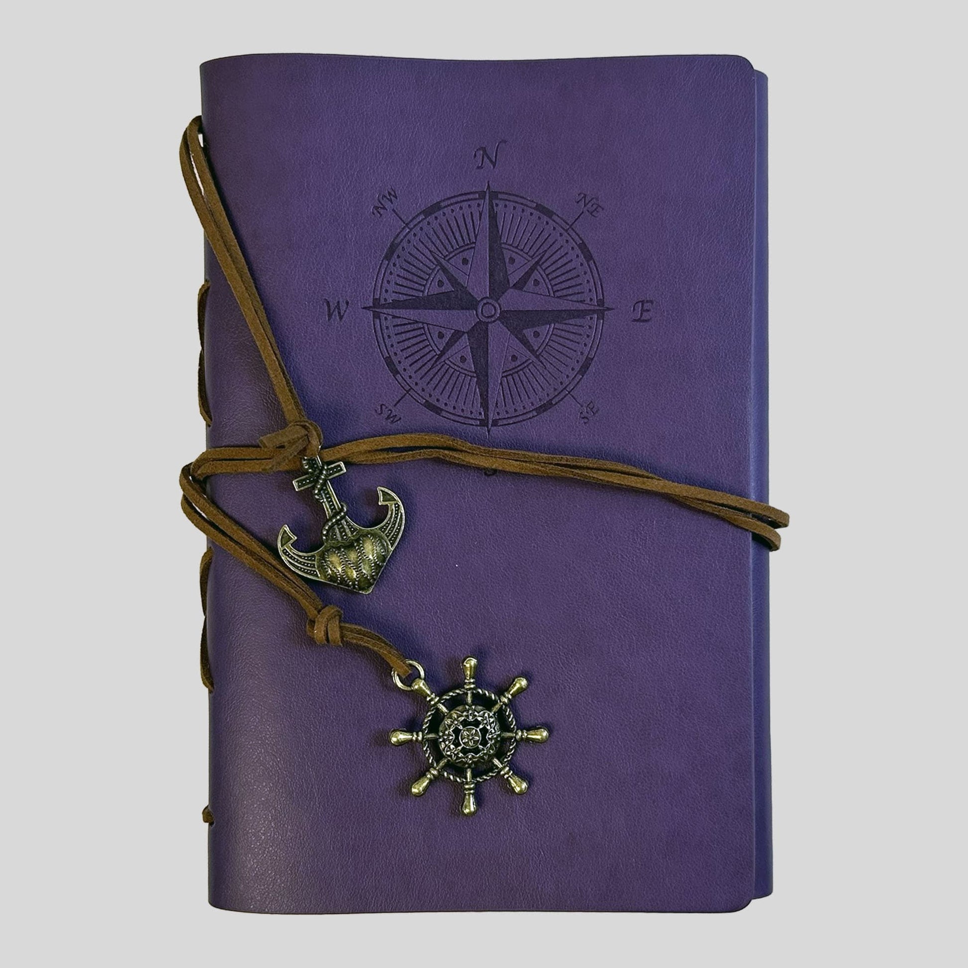 A professional product shot of a vibrant purple faux-leather journal from the Fehmerling Books standalone collection. The screen showcases an embossed compass rose on the cover, wrapped in brown twine and accented with antique gold-toned anchor and ship wheel charms. This high-quality image captures a mystical and adventurous aesthetic, perfect for creative writing and personal reflections.