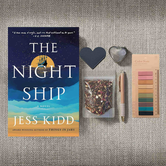 A product image for the "Reader Retreat Bundle" showcasing the New condition paperback of "The Night Ship" alongside expanded reading accessories. In addition to the heart-shaped bookmark, muted annotation tabs, and a rose-gold pen, this set includes a heart-shaped metal tea infuser and a clear packet of floral loose-leaf tea.
