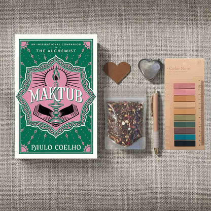 Dark academia bookish flatlay of Paulo Coelho's 'Maktub' with herbal tea, stationery, and vintage-style reading accessories on a textured background.