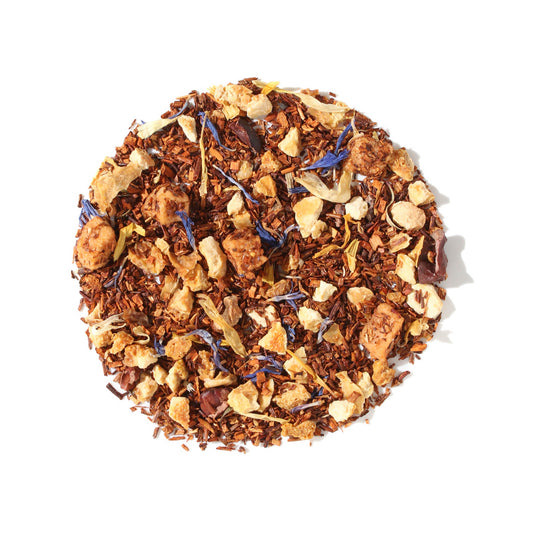 A close-up, overhead view of Plum Deluxe Soul Warmer Herbal Tea arranged in a neat circle against a white background. The loose leaf blend features fine red rooibos needles mixed with visible chunks of apple, dark cocoa nibs, and colorful pops of calendula and cornflower petals.