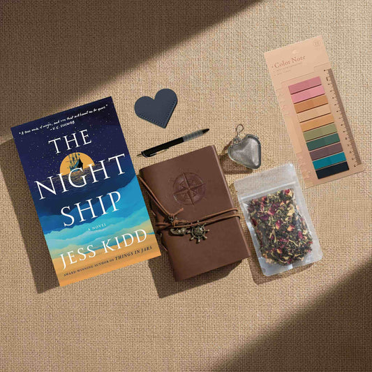 The "Ultimate Bundle" product photo features an overhead view on a tan textured surface, including "The Night Ship" paperback and a premium brown leather journal embossed with a compass rose. The comprehensive set includes all retreat elements—loose-leaf tea, a heart tea infuser, a heart bookmark, and annotation tabs—accented by a nautical-themed charm tied to the journal's leather strap.