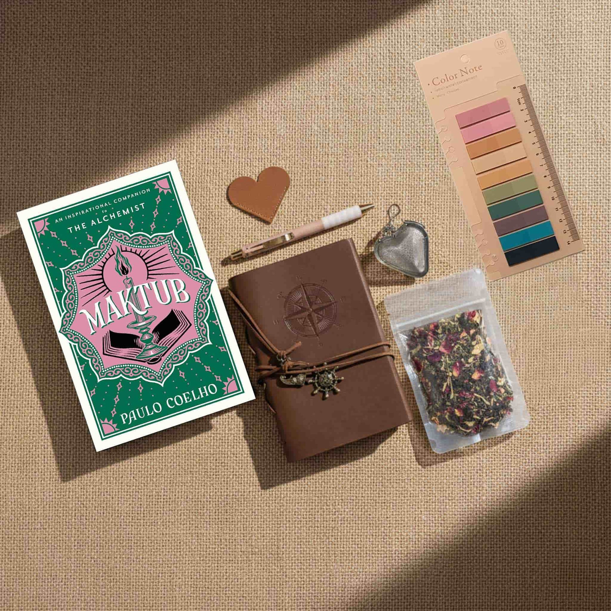 Dark academia aesthetic flatlay of the book Maktub, aesthetic color palette sticky notes, a vintage-style pen, and dried herbal tea on a neutral textured background.